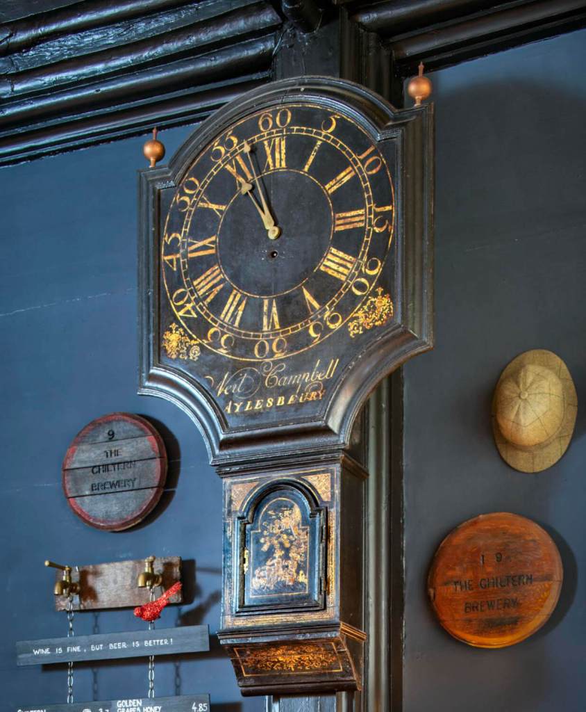 Photograph of a wooden tavern clock, with gold detailing, gold hands and roman numerals. 