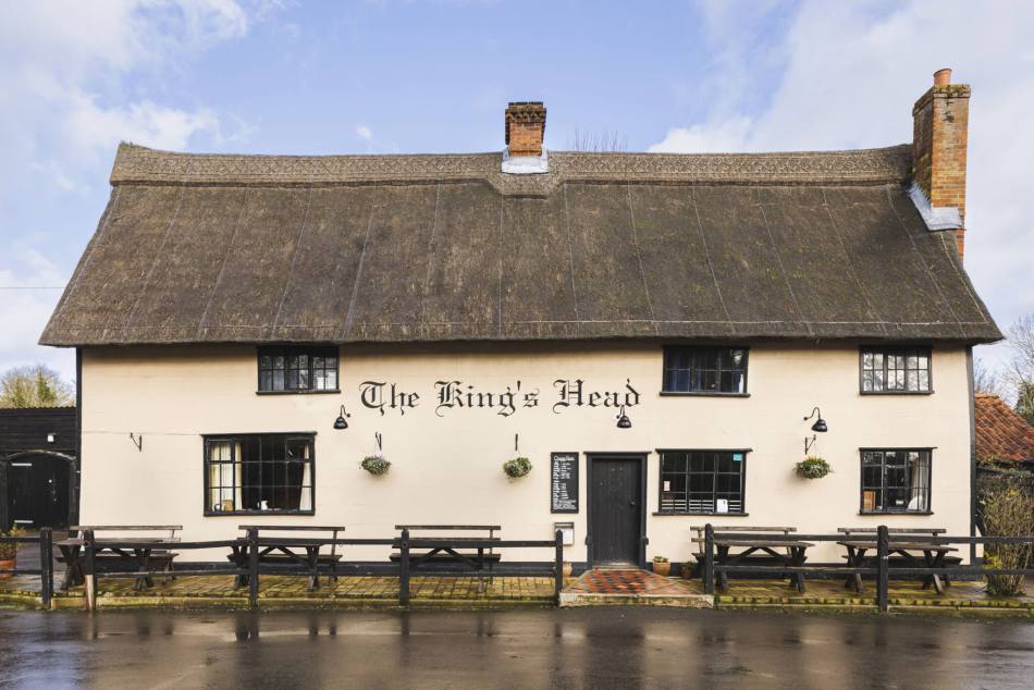 A cream coloured, thatched roof pub with some tables and benches outside.