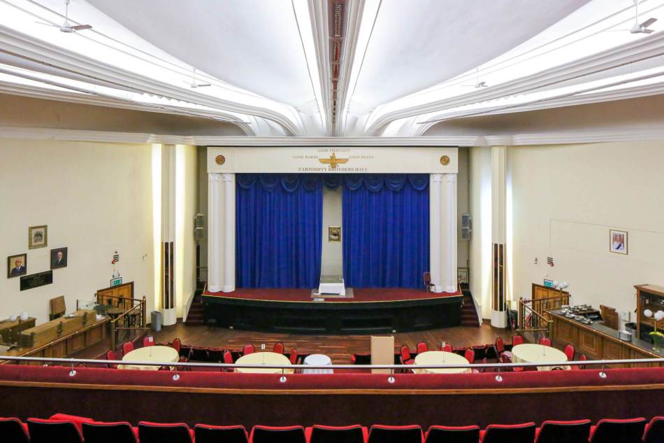 The interior of a converted historic cinema, looking towards the stage/screen area, at the top of which are Zoroastrian symbols.