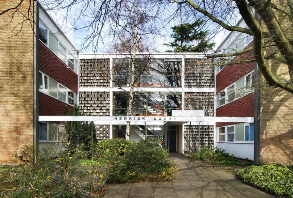 Exterior view of 3-storey Modernist housing block, where windows look out over planted flower beds and the building entrance.
