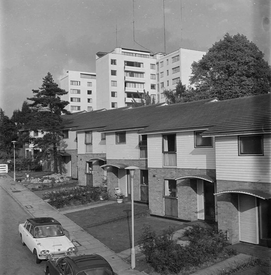 Black and white archive image of a terrace of houses with a group of tall white apartment buildings in the background.