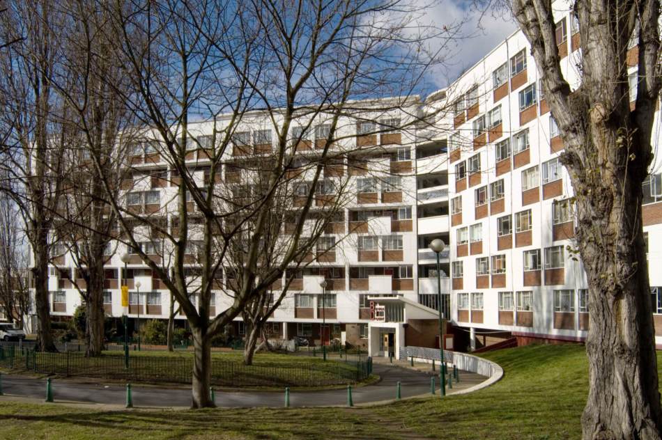 A colour photograph of blocks of flats with adjacent access road and lawns.