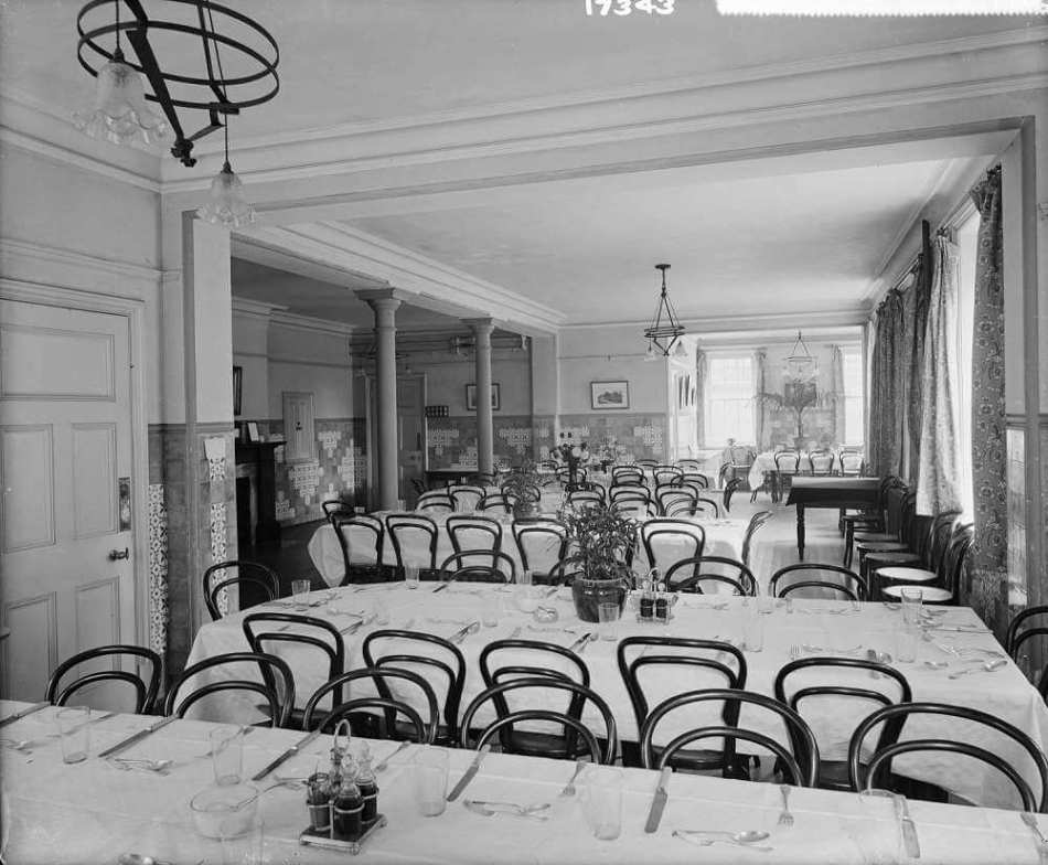 A black and white archive image of a large, partly tiled dining room with rows of tables and chairs.