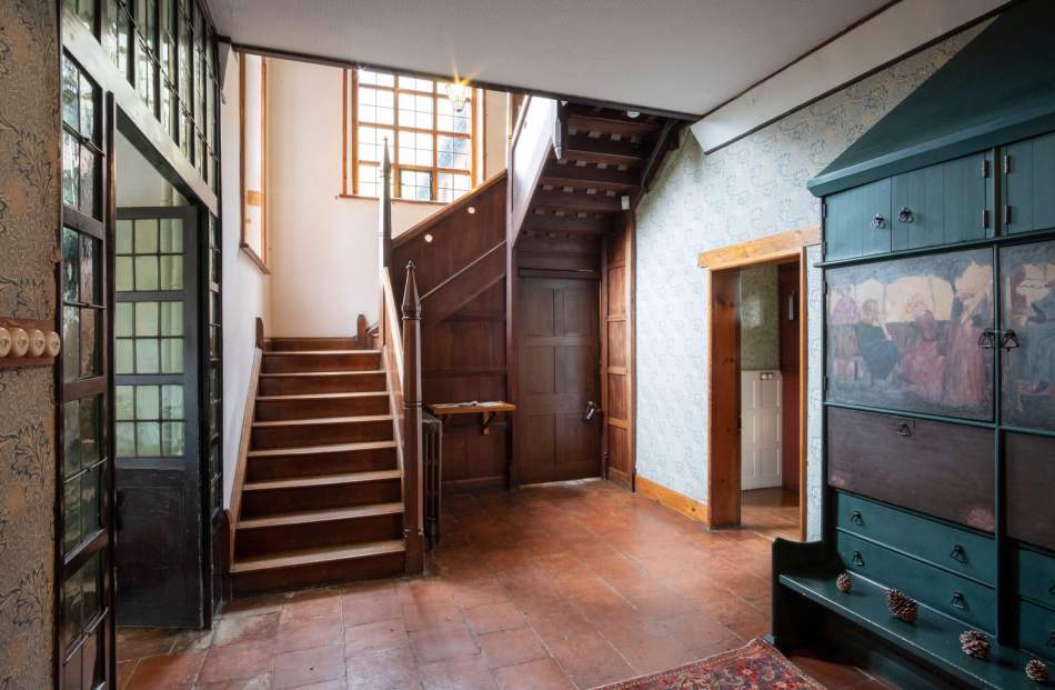A photograph of the interior of a house, showing the hallway and stairwell decorated in an Arts and Crafts style.