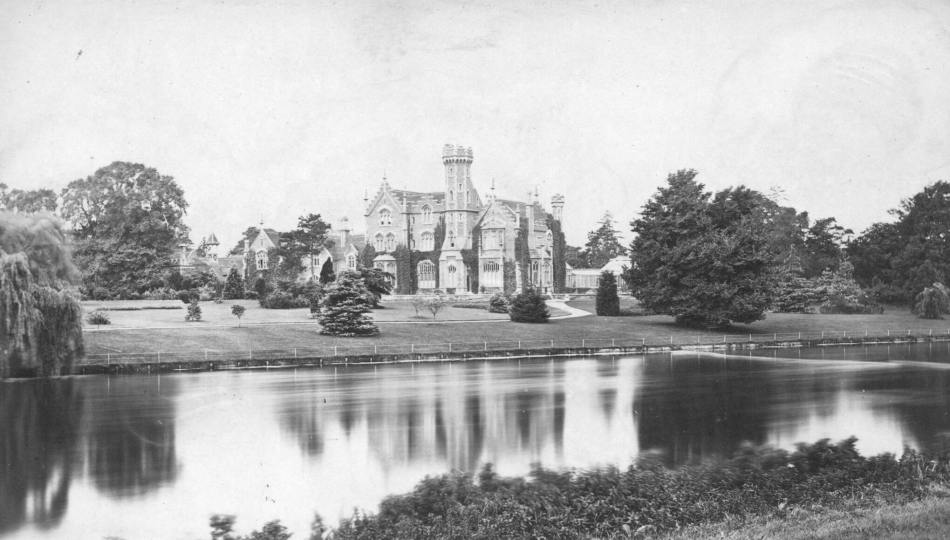 A black and white archive image of a gothic mansion with a river in teh foreground.