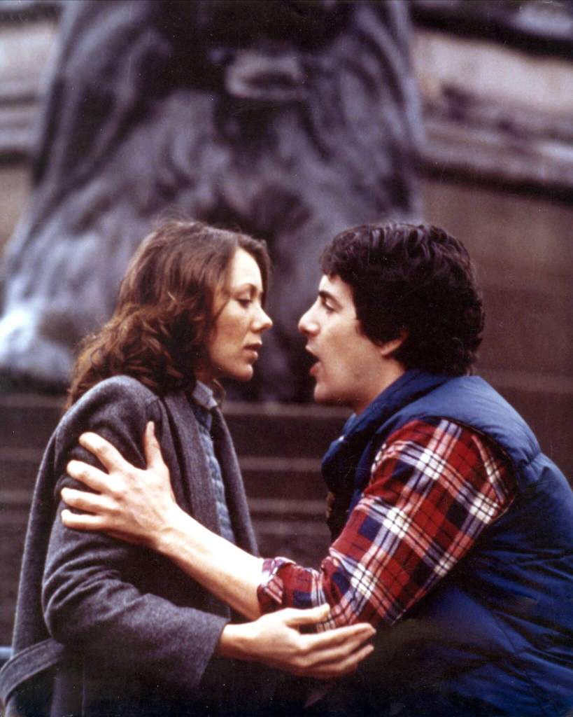 A still from a film showing an actress and  actor embracing with the base of a monument in the background.