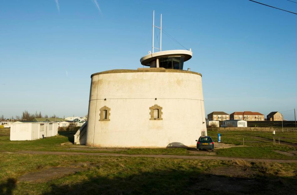 A photograph of a white Martello tower with two small windows sitting within a field. 