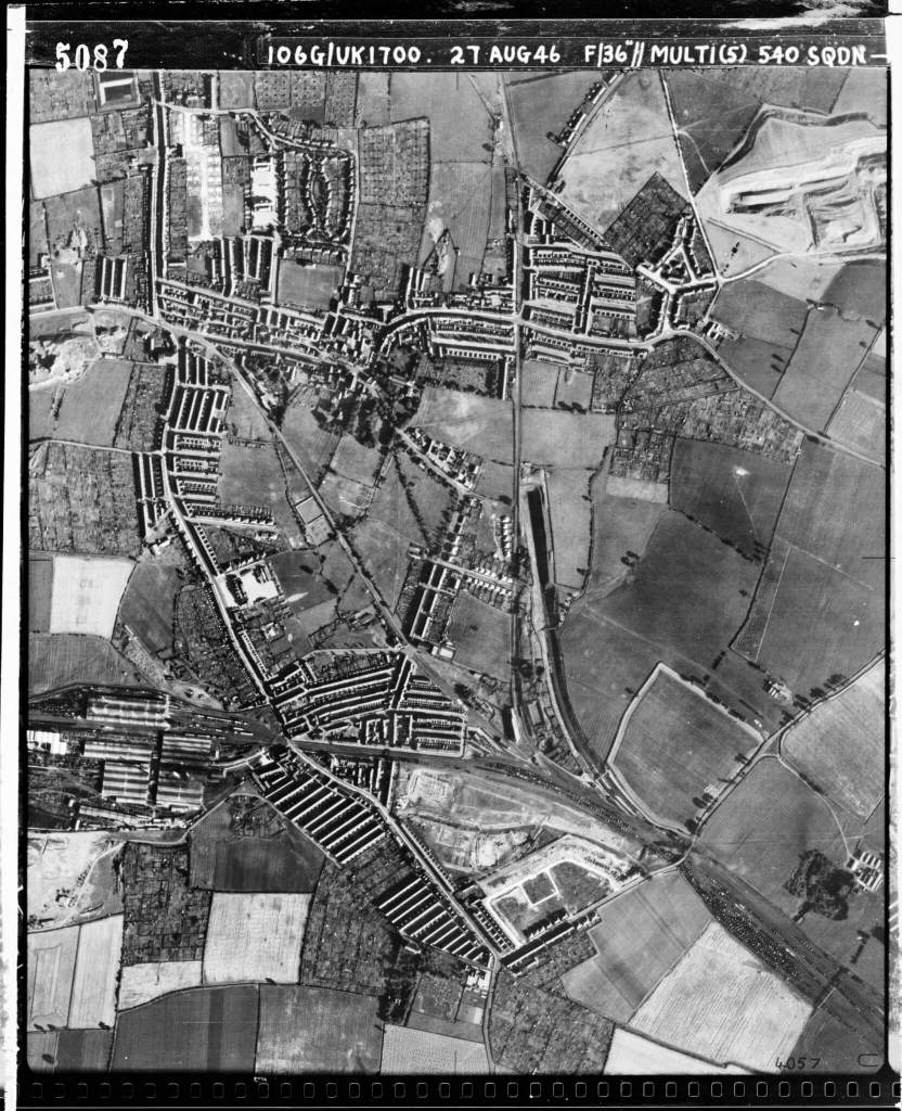 A black and white aerial photograph of a village surrounded by farmland.