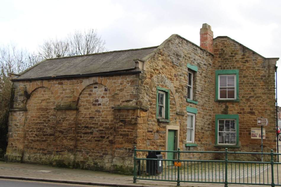 A photograph of a stone, 2-storey cottage with bright green painted doors and window surrounds.