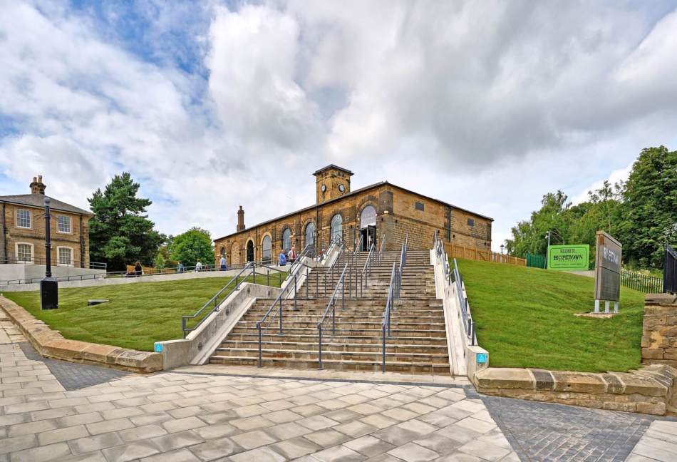 A photograph of a large. external stone staircase leading up to a renovated industrial building with a small clock tower at the centre.