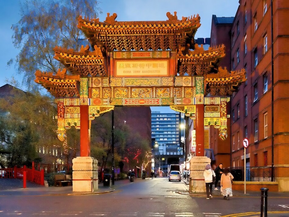 A vividly decorated Chinese archway on an urban street. A few pedestrians walk beneath the arch.