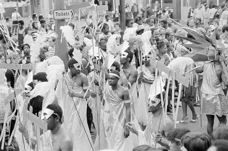 A black and white photograph of people dressed in costume in a street carnival. 