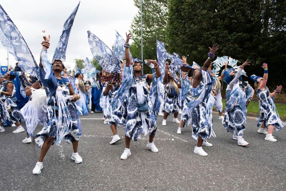 A photograph of people in fancy dress dancing in a street carnival. 