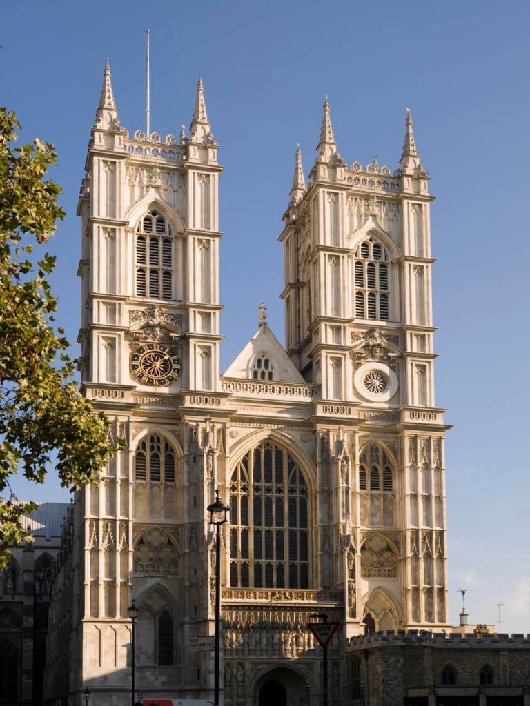 A photograph of facade of Westminster Abbey, showcasing its intricate Gothic architecture, tall spires, and detailed stonework against a clear blue sky.