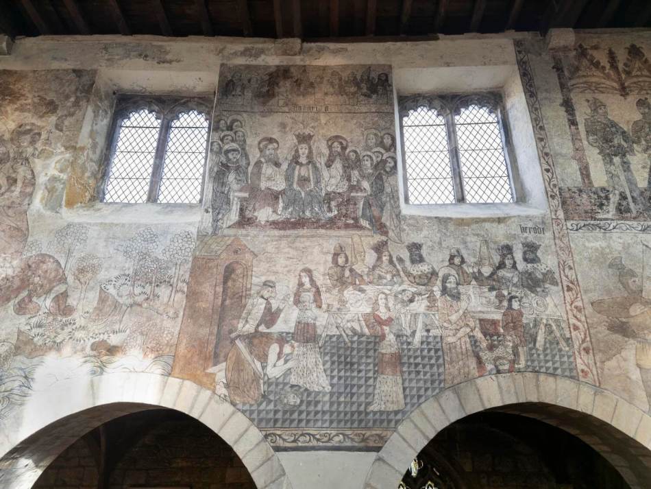 A photograph of the interior wall of a church nave covered in medieval wall paintings.