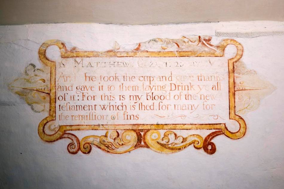 A close-up photograph of a wall painting of some text from a gospel, surrounded by an elegant painted frame.