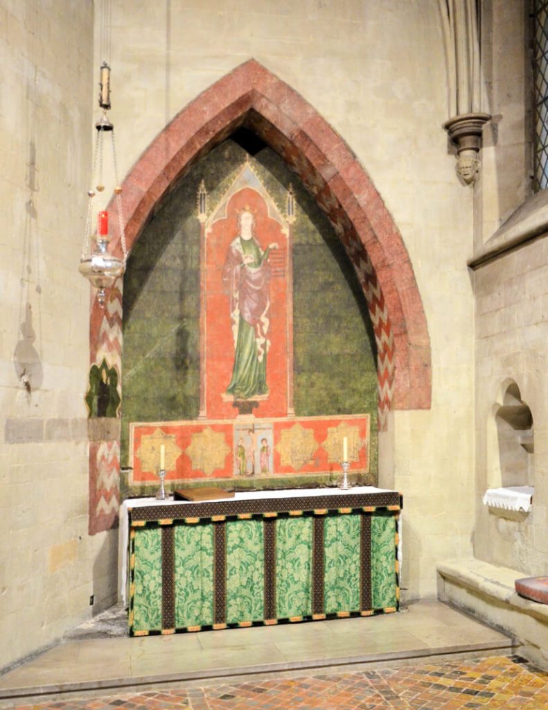 A photograph of the interior of a chapel featuring a large wall painting of a crowned figure standing beneath a canopy.