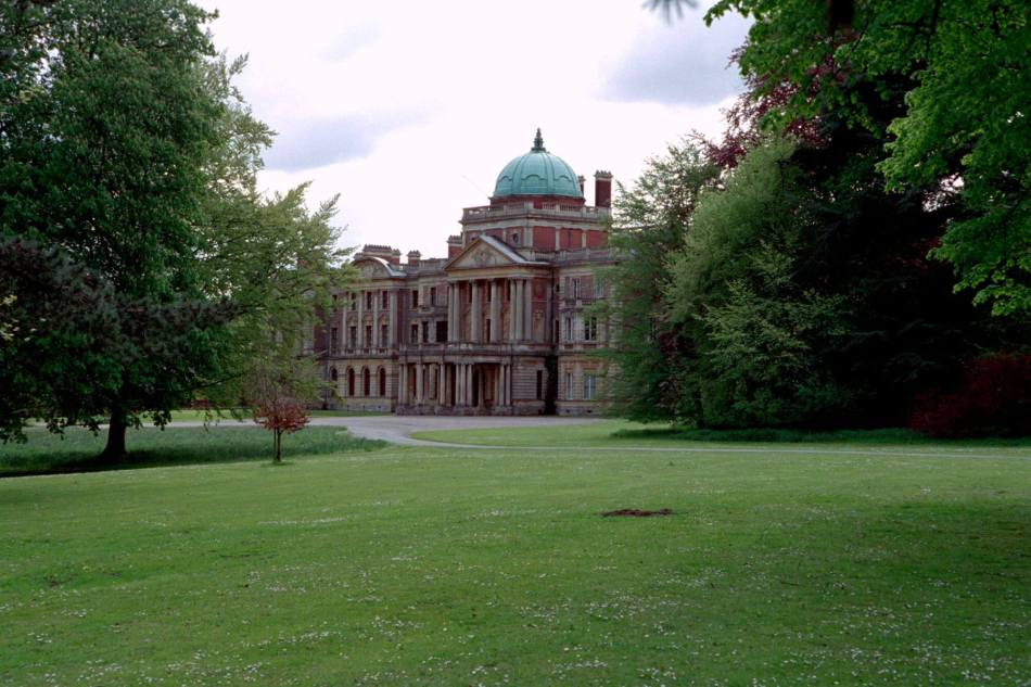 A photograph of a large, stately home surrounded by large trees and parkland.