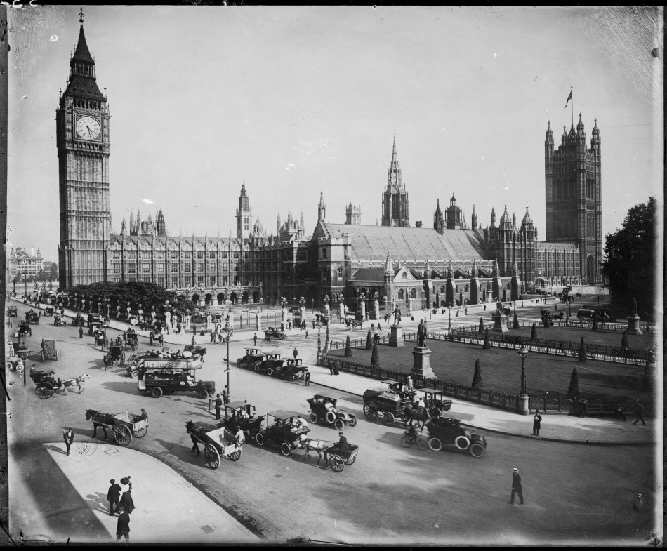 A black and white photograph showing Big Ben and the Houses of Parliament, with the roads surrounding the buildings filled with vintage cars and horse-drawn carriages.