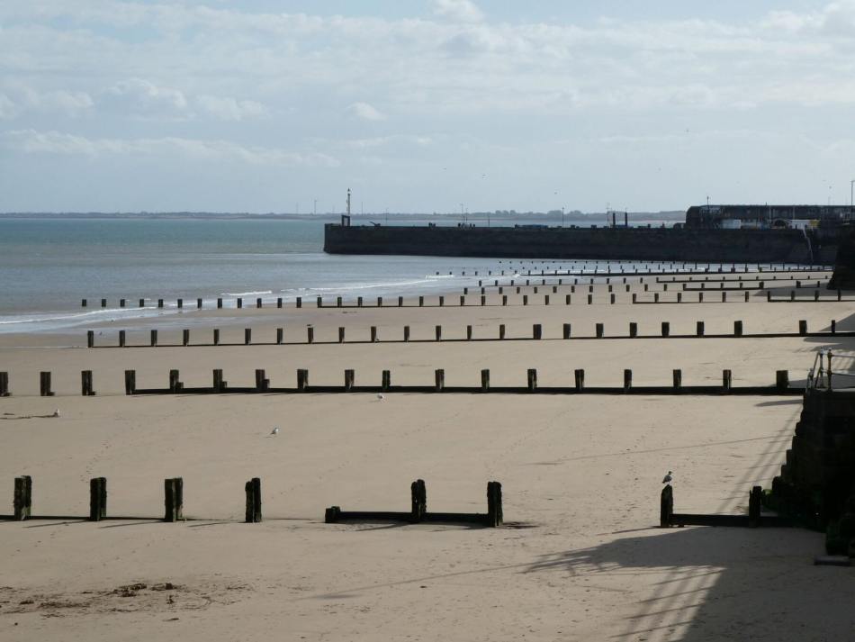 A photograph of a beach with a small pier in the distance.