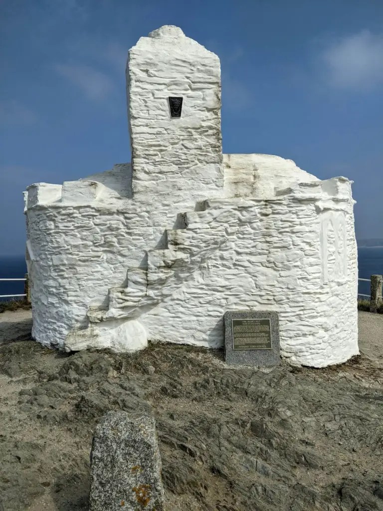 A photograph of a small, single-storey stone rubble building in a circular shape, painted white. There is a small tower at the centre.