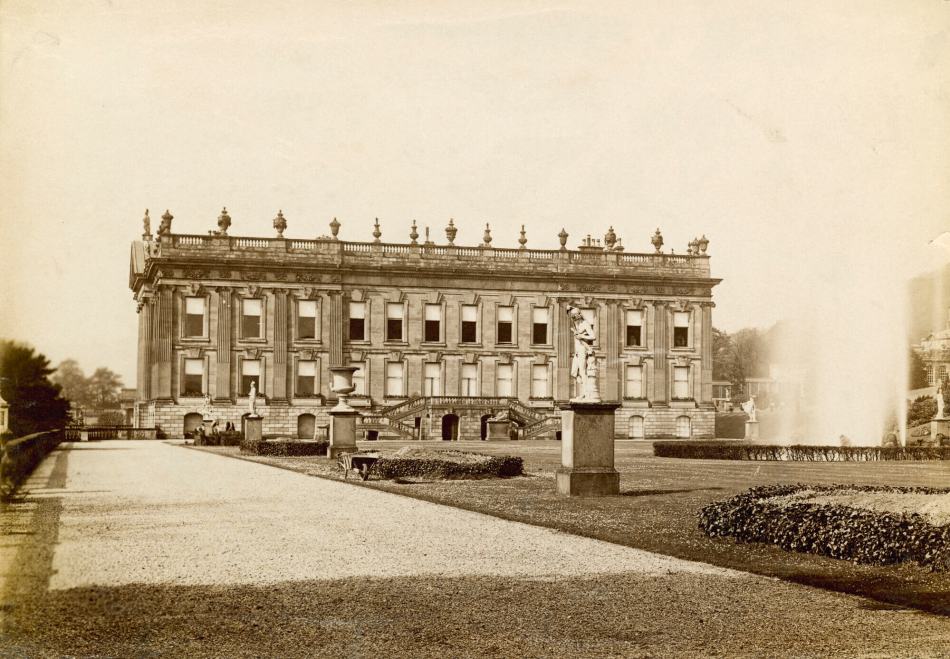 A sepia photograph of the exterior of a large country house featuring Baroque and Neo-classical design styles surrounded by ornamental gardens.