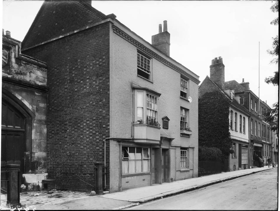 A black and white photograph of a 3-storey townhouse beside a road.