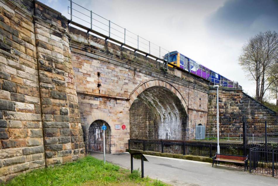 A photograph of a stone railway bridge with a small train travelling over the top of it.