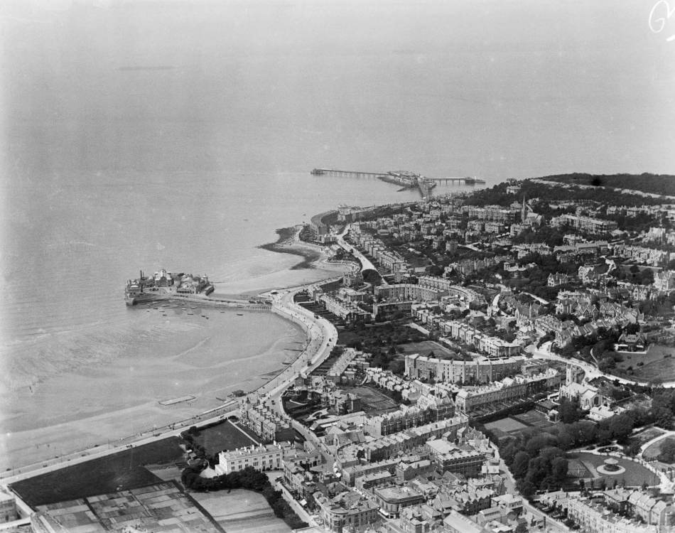 A black and white aerial photograph of a seaside town with a large pier in the background.