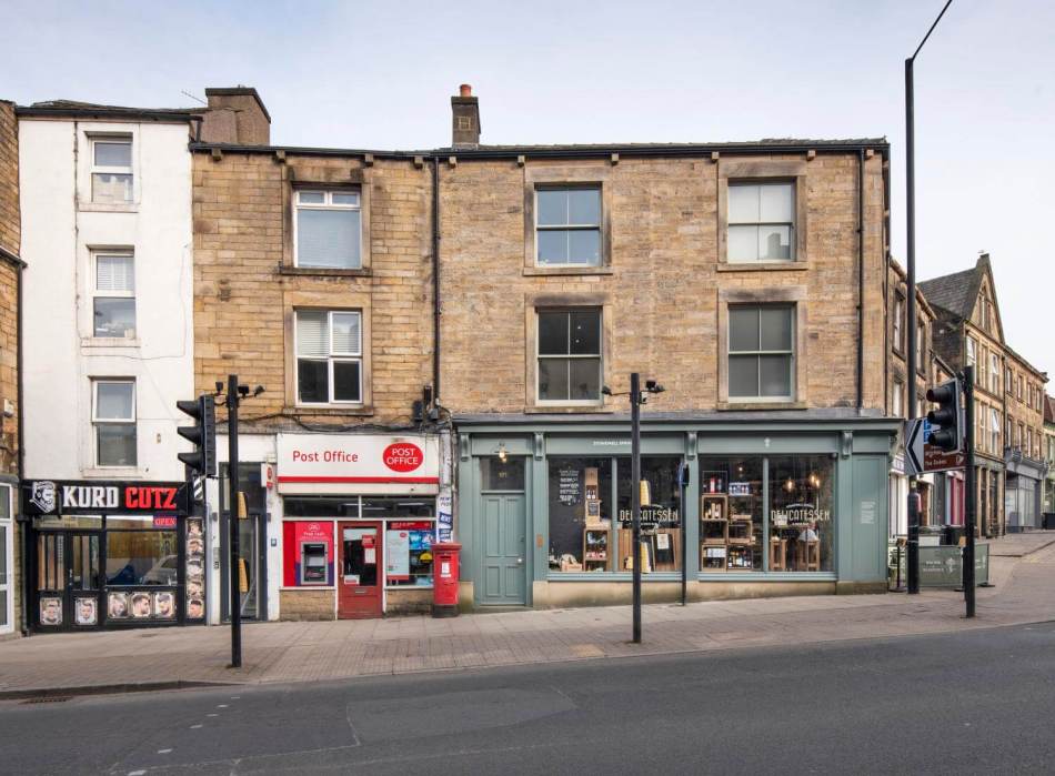 A photograph of a row of 3-storey traditional stone buildings with a post office and a delicatessen on the ground floors.