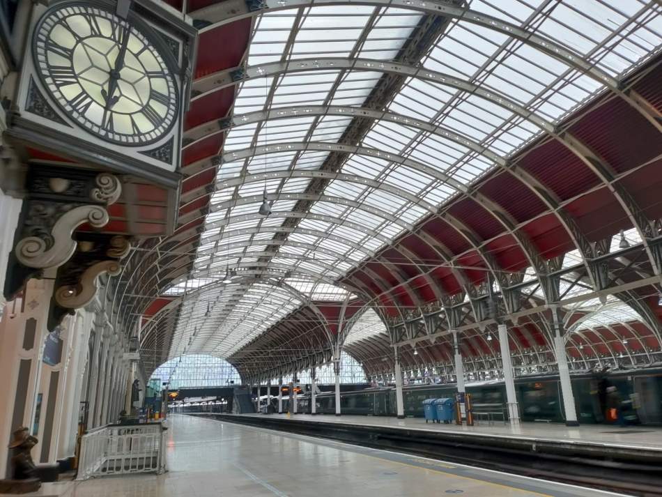 A photograph of the interior of a large railway building with a curved ceiling and a large, ornate clock on the wall beside the platform.
