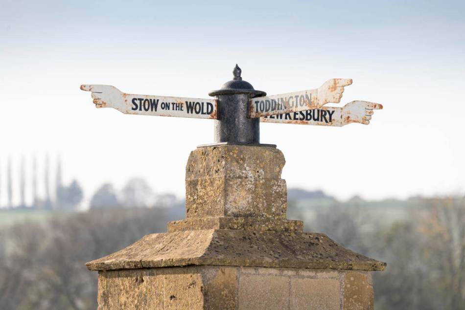A photograph of a metal fingerpost pointing in 3 different directions on top of a stone plinth.