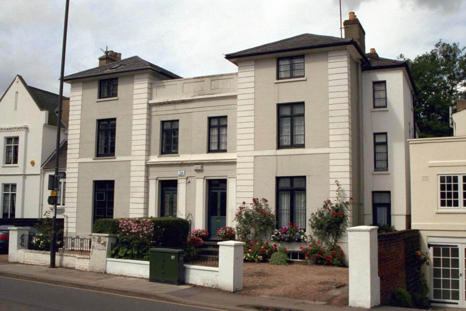 A photograph of the exterior of 2 3-storey, semi-detached neo-classical villas with front gardens beside a road.
