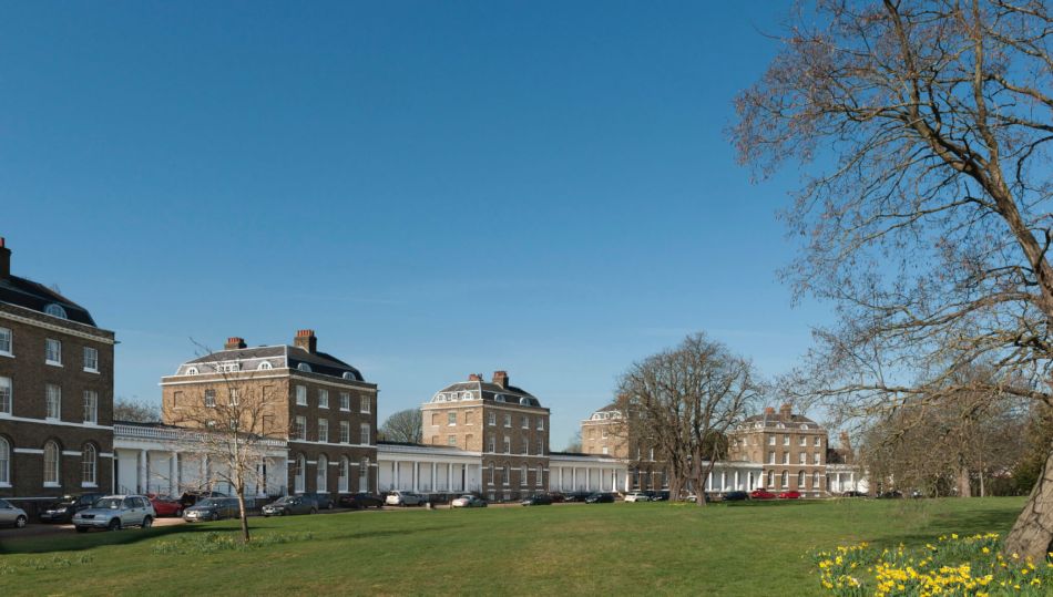 A photograph of a crescent of 5 blocks of grand, 4-storey semi-detached houses overlooking a road and a large green space with trees.