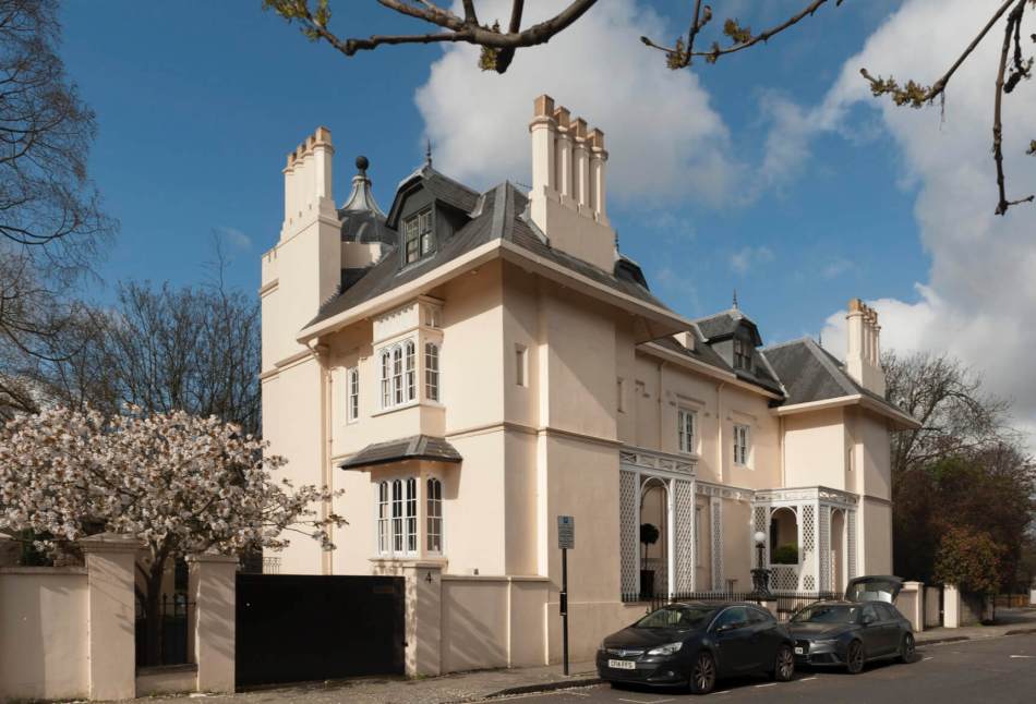 A photograph of the exterior of a large, semi-detached Italianate villa with numerous tall chimney stacks.