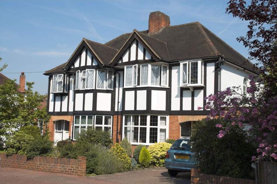A photograph of the exterior of 2 mock Tudor-style semi-detached houses with timber-frames and small front gardens.
