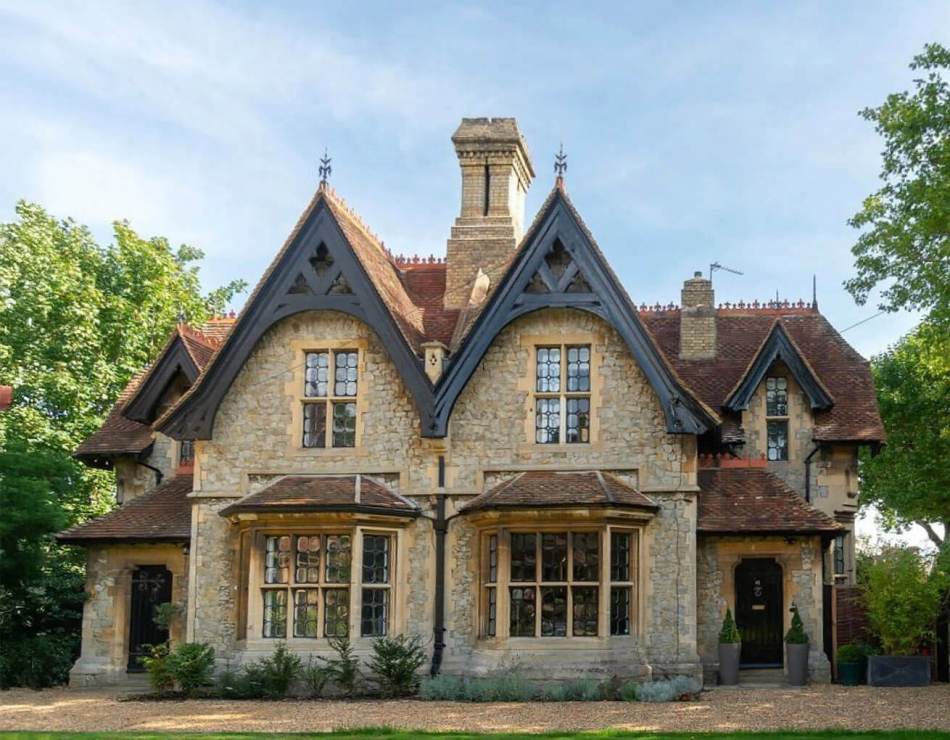 A photograph of the exterior of 2 Gothic Revival-style semi-detached houses surrounded by a gravel path, grass and trees.