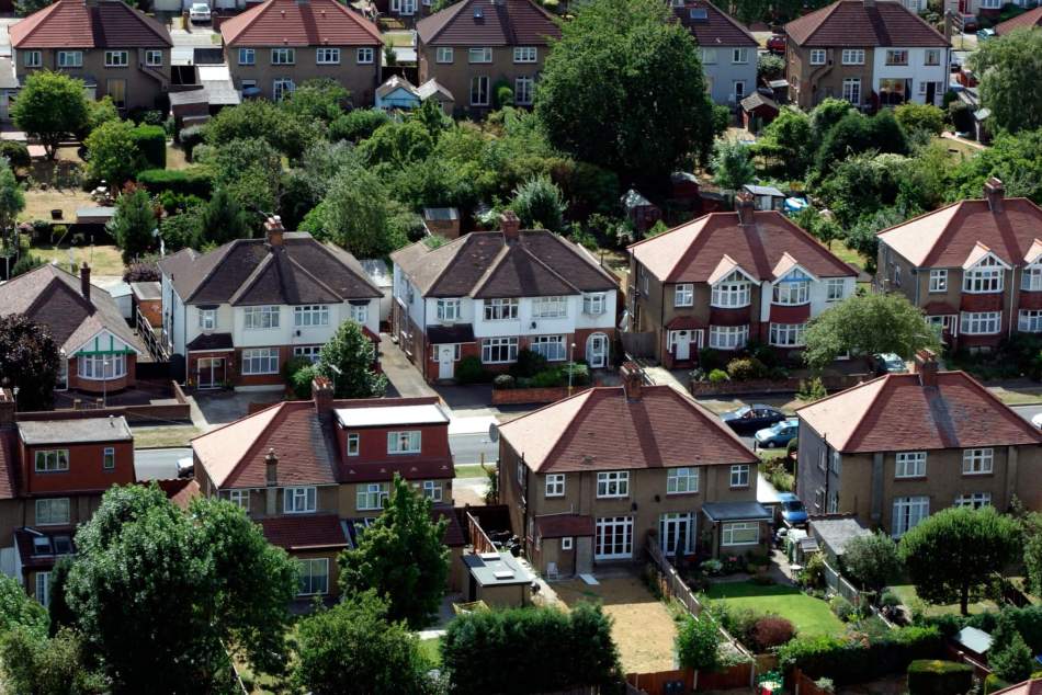 An aerial photograph of rows of semi-detached houses with large gardens in a suburb of a city.