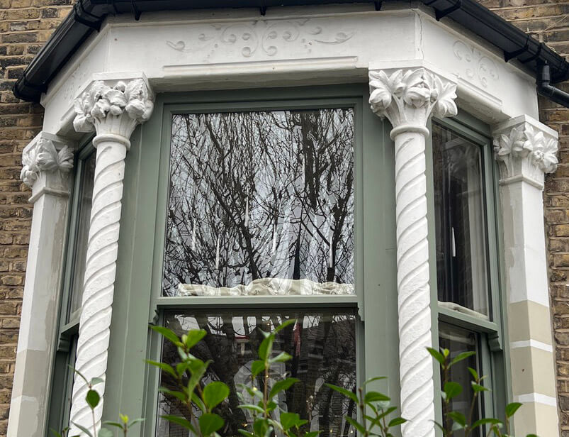 A photograph of the exterior of a highly decorative bay window with stone capitals adorning the edges of the windows.