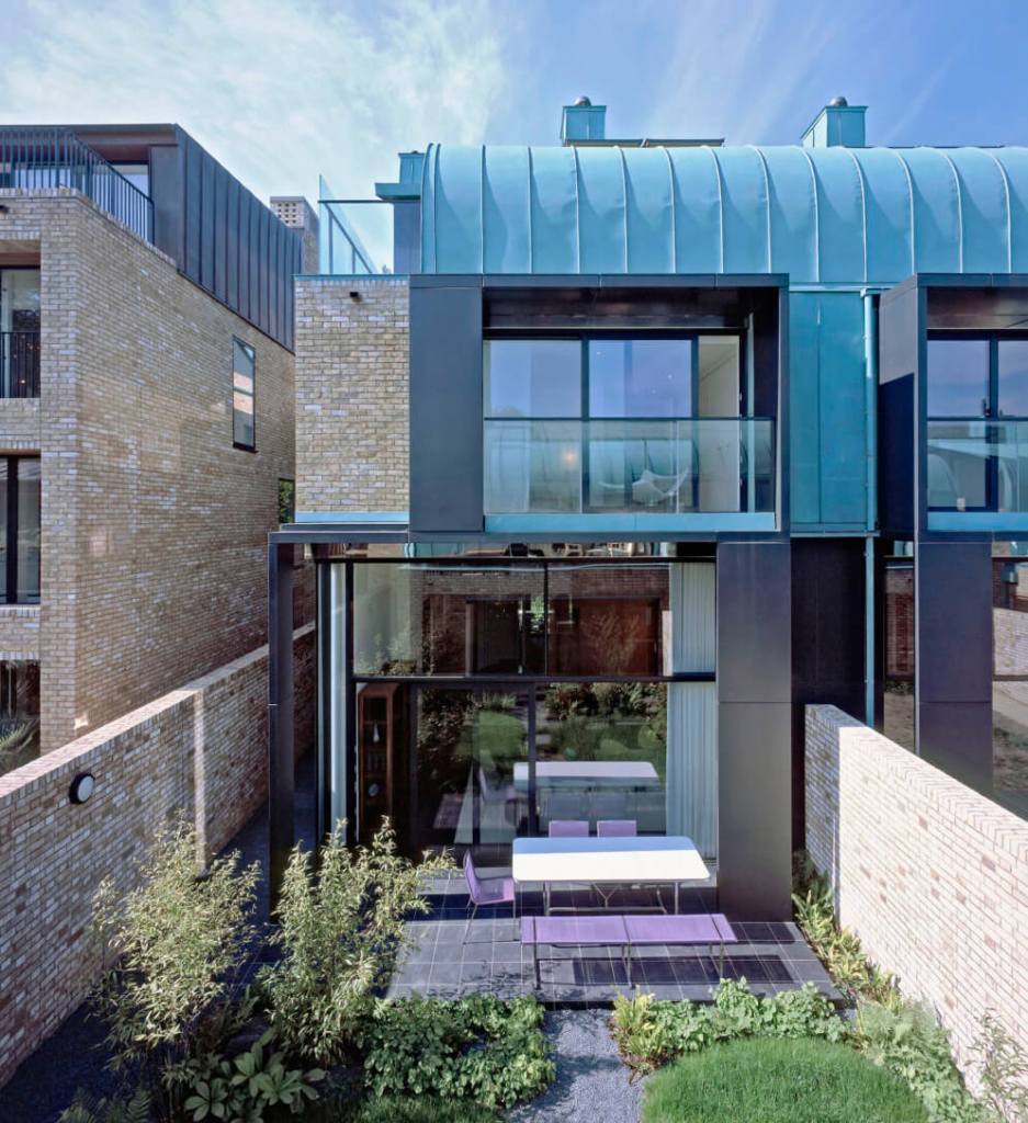 A photograph of the exterior of the back of a modern semi-detached house with large. floor to ceiling windows on the ground floor, with a glass balony on the first floor, and a metal panelled  roof.