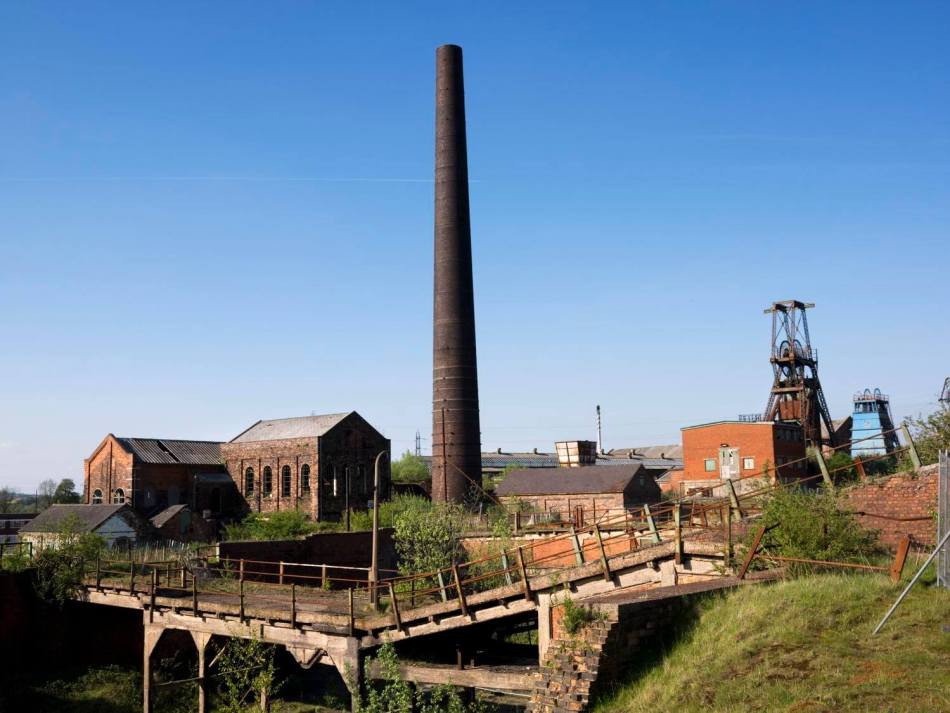 A photograph of a disused colliery yard with a tall chimney at the centre surrounded by various warehouses and machinery.