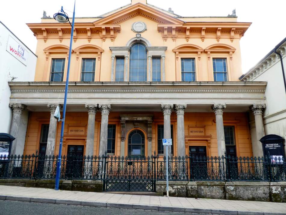 A photograph of the exterior of a Methodist chapel with a stuccoed Italianate frontage with Corinthian columns. Ornate iron railings surround the entrance to the building.