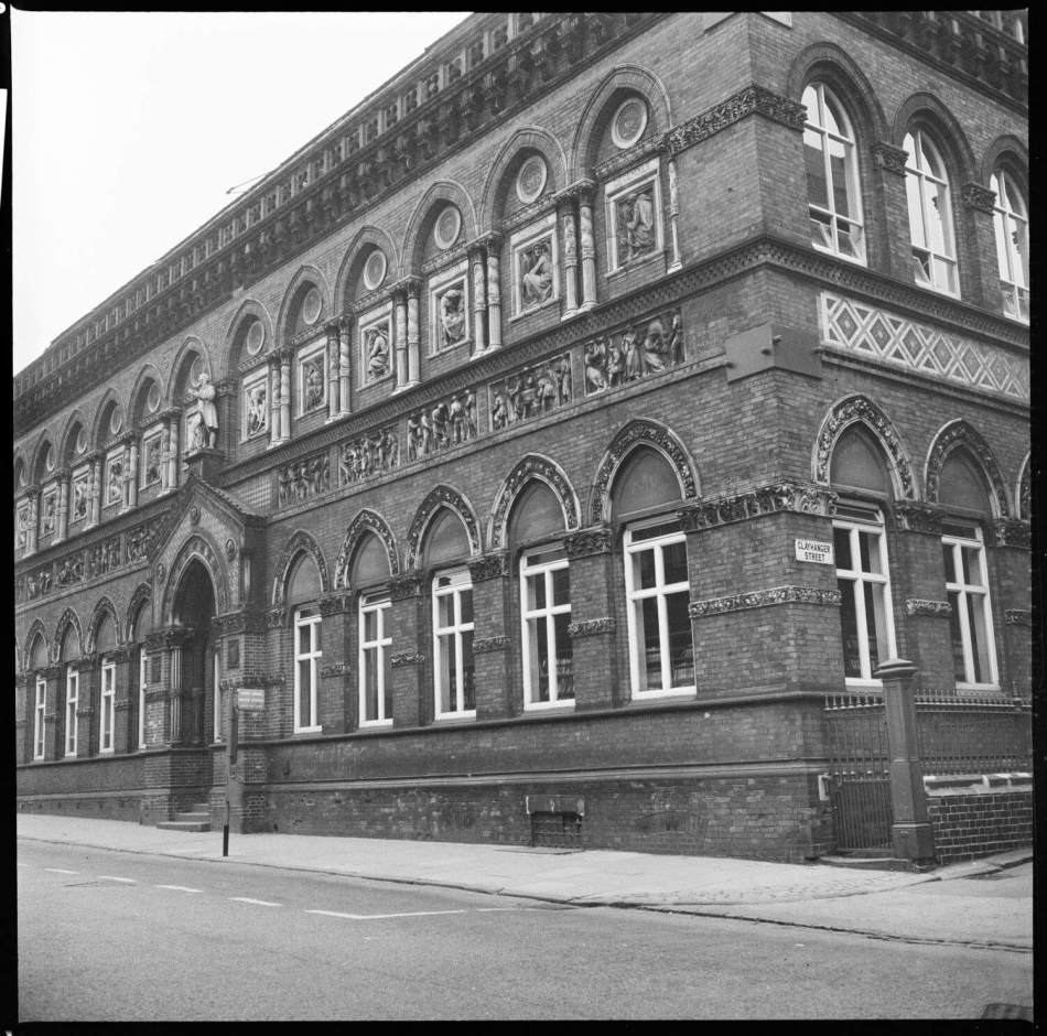 A photograph of the exterior of a large public building with a richly ornamented facade with a gabled porch enriched with terracotta frieze.