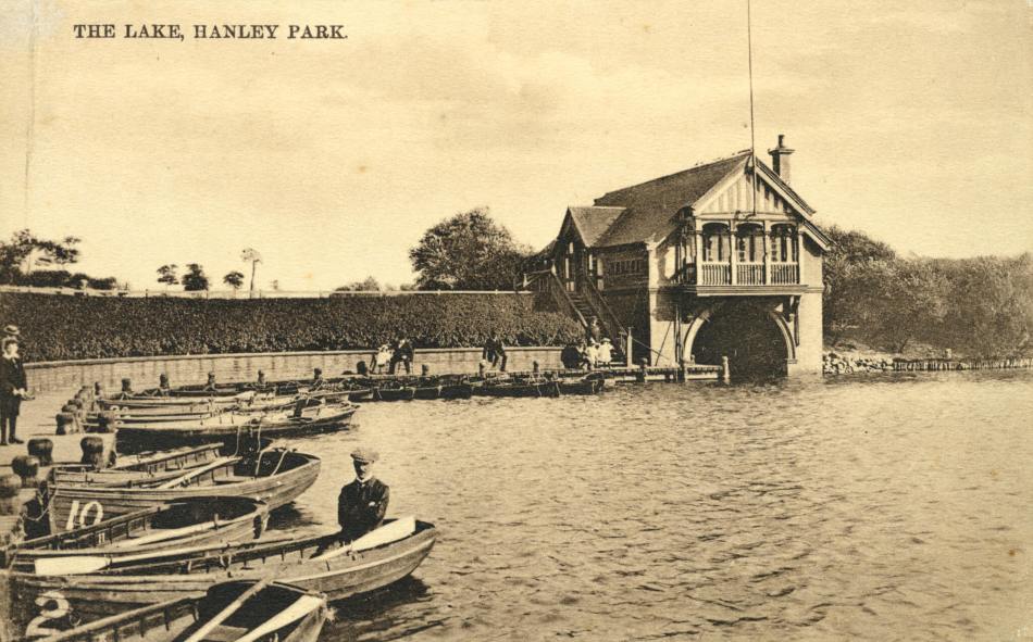A sepia photograph of a boathouse beside a lake, with small boats lined up beside a pathway.