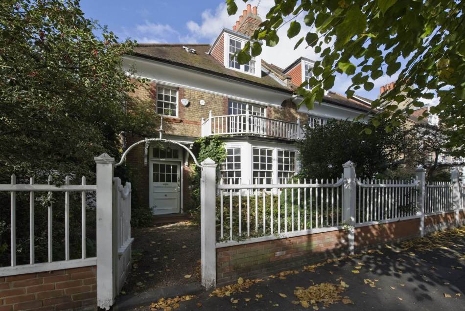 A photograph of the exterior of a semi-detached house with white fencing and a gate in front of the front garden.