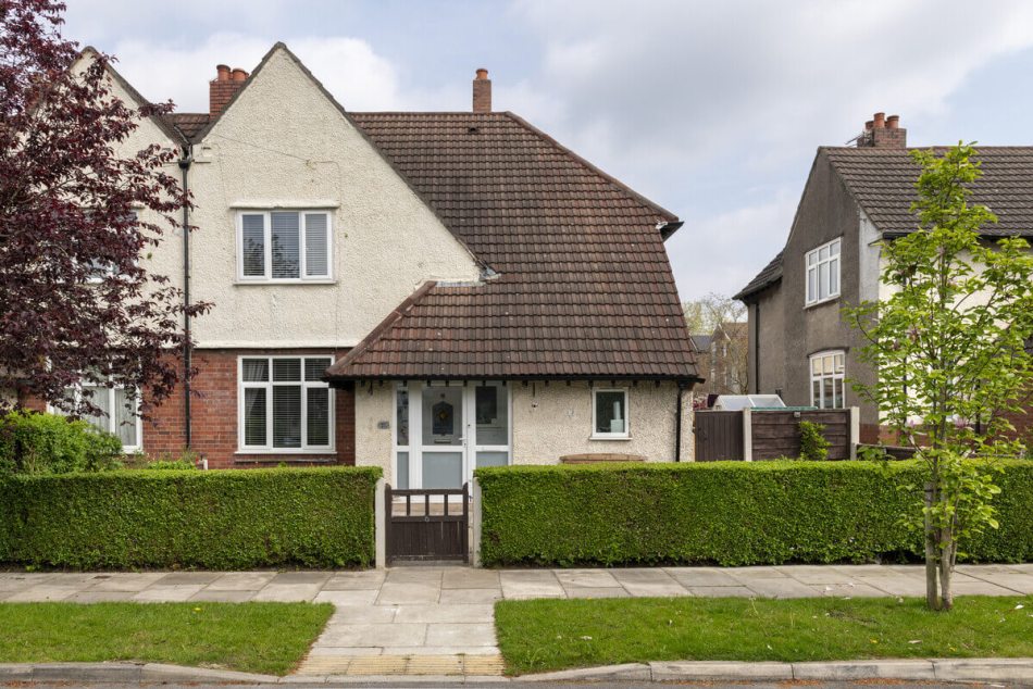 A photograph of the exterior of a semi-detached house with a front garden surrounded by an ornamental shrub as a fence.
