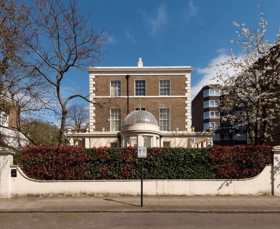 A photograph of the exterior of a pair of Georgian-style semi-detached houses with a circular, glazed conservatory with glass dome and pineapple finial at the centre.