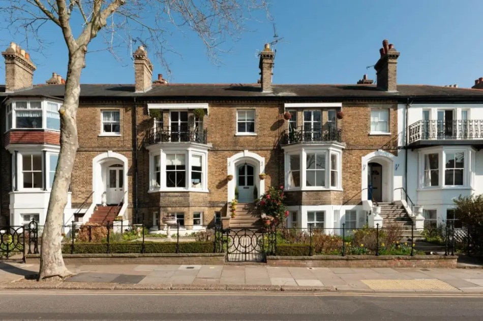A photograph of a row of terraced housing with steps up to the entrance, bay windows on the first floor, and balconies in front of the large windows on the top floor.