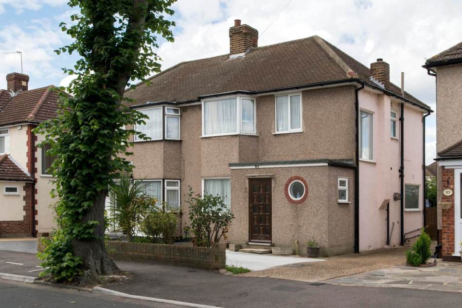 A photograph of the exterior of a pair of semi-detached pebble dash houses beside a pavement.
