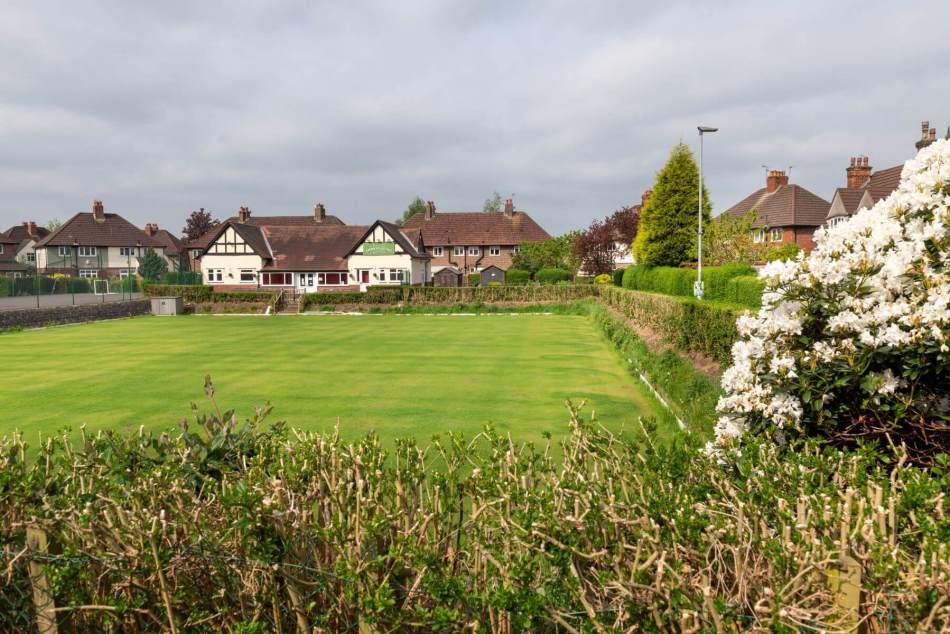 A photograph of a sports field with a community sports hall and housing in the background.